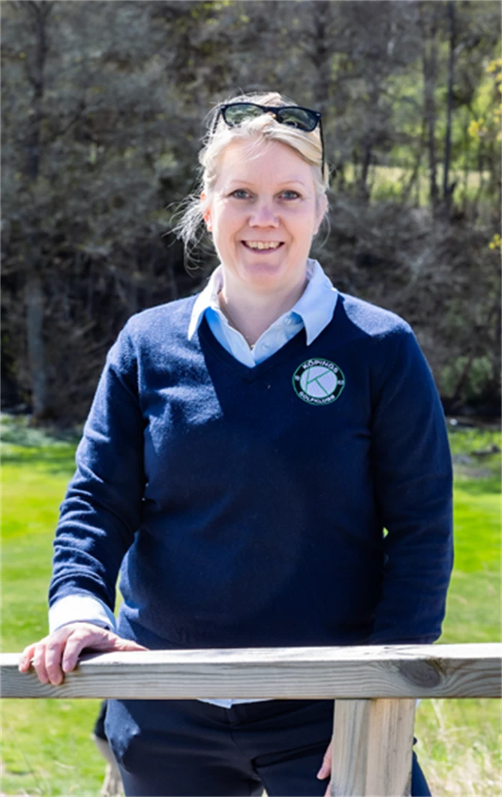 Bild på Lena Björkdahl som är klubbchef för Köpings Golfklubb. Hon står utomhus vid golfbanan.