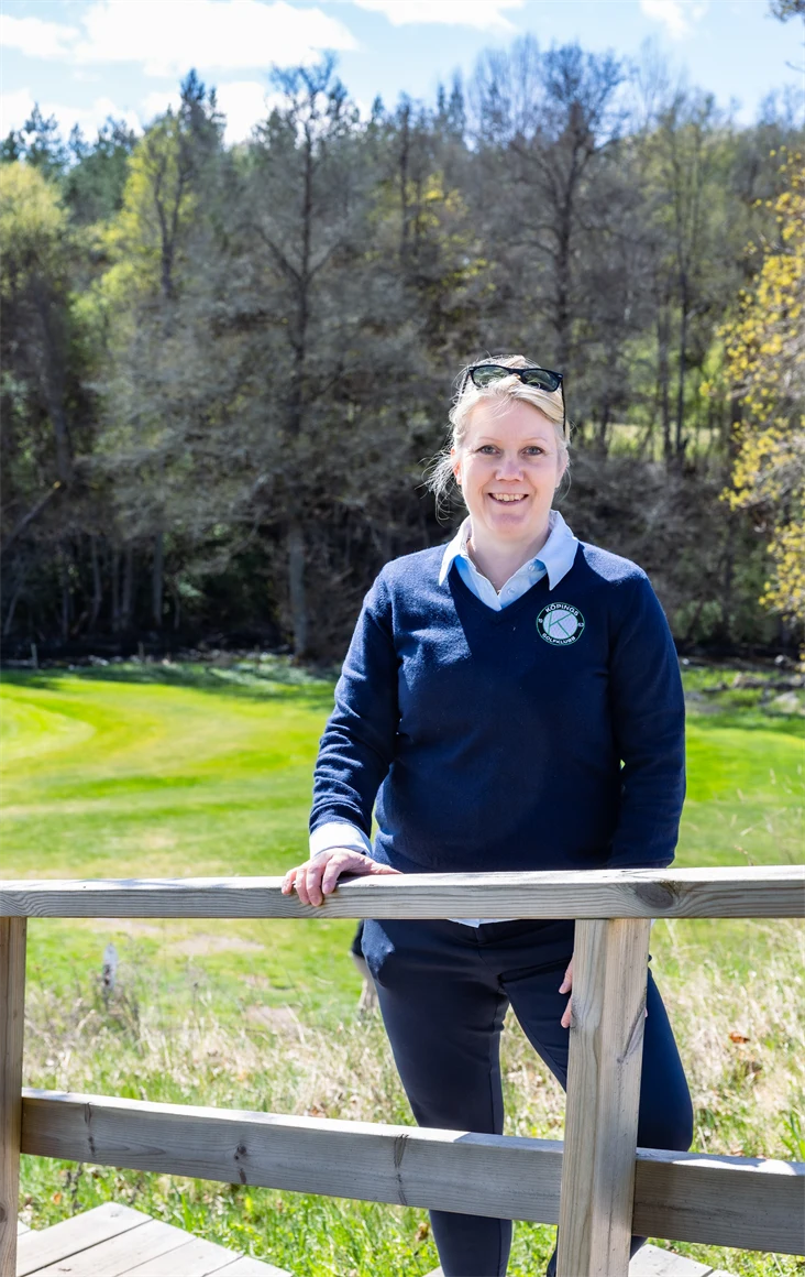 Bild på Lena Björkdahl som är klubbchef för Köpings Golfklubb. Hon står utomhus vid golfbanan.