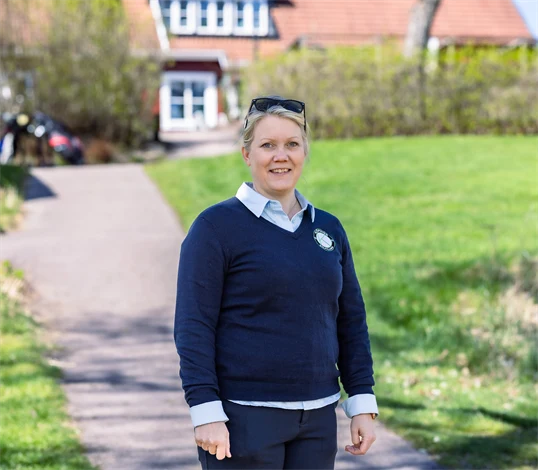 Bild på Lena Björkdahl som är klubbchef för Köpings Golfklubb. Hon står utomhus utanför golfklubben.